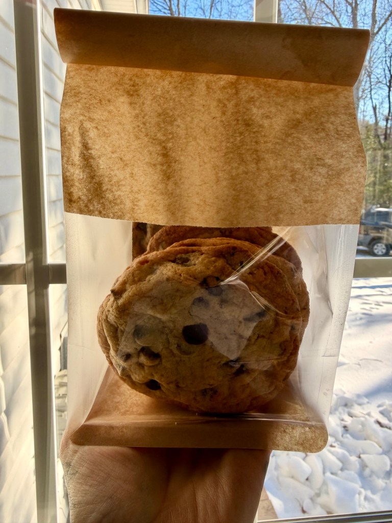 A brown Kraft bag with five large chocolate chip cookies.